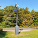 Marlec Rutland 1200x Land-Based Wind Turbine with MPPT Controller 12V with solar panel on a grassy area with trees in the background