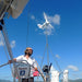 Man on a sailboat with a wind turbine against a blue sky
