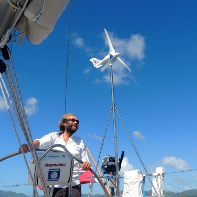 Man on a sailboat with a wind turbine against a blue sky